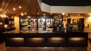 Zona de bar con mostrador, estantes con botellas, vasos y una máquina de café.