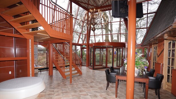 Un espacio interior amplio con una escalera de madera, una mesa de comedor con sillas y un objeto circular blanco en el suelo.