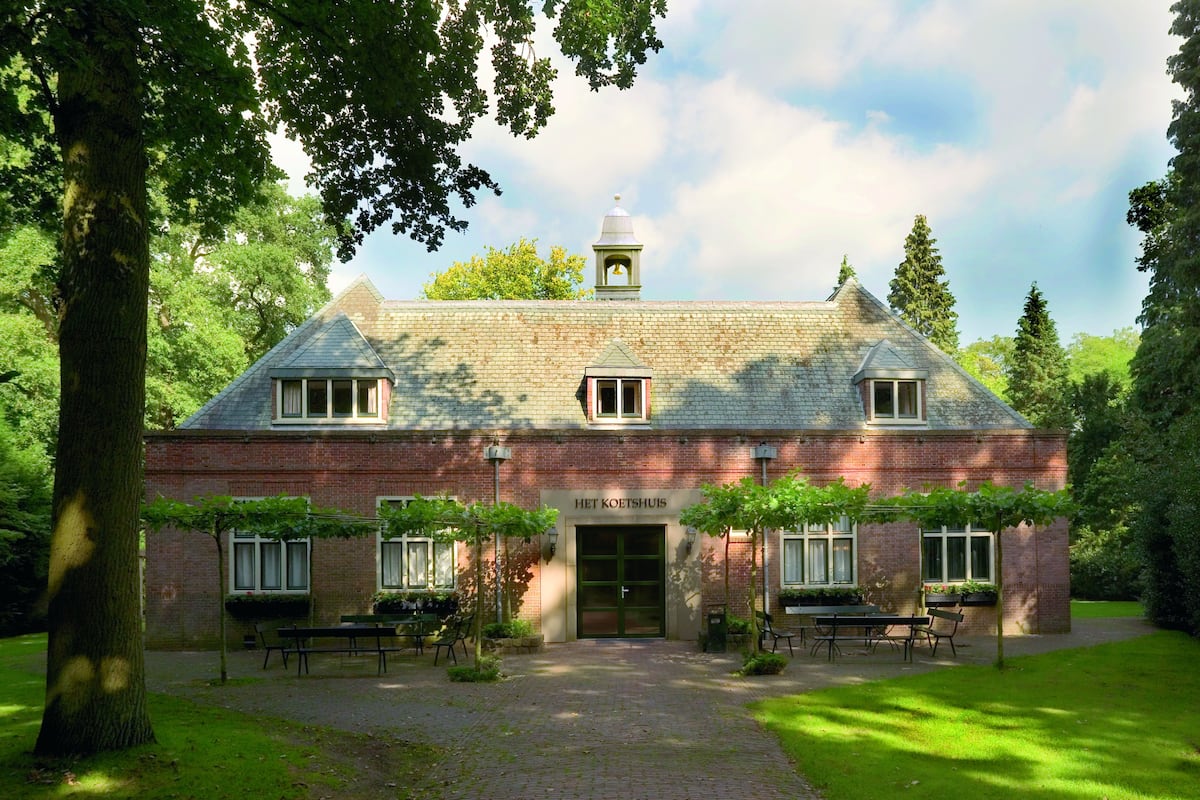 A brick building with a central entrance, a bell tower, and a garden area with benches and tables.