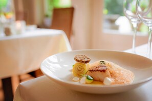 A white plate with a piece of fish, a small round item, and some green garnish on a table. - Landgoed Huize Bergen (Vught)