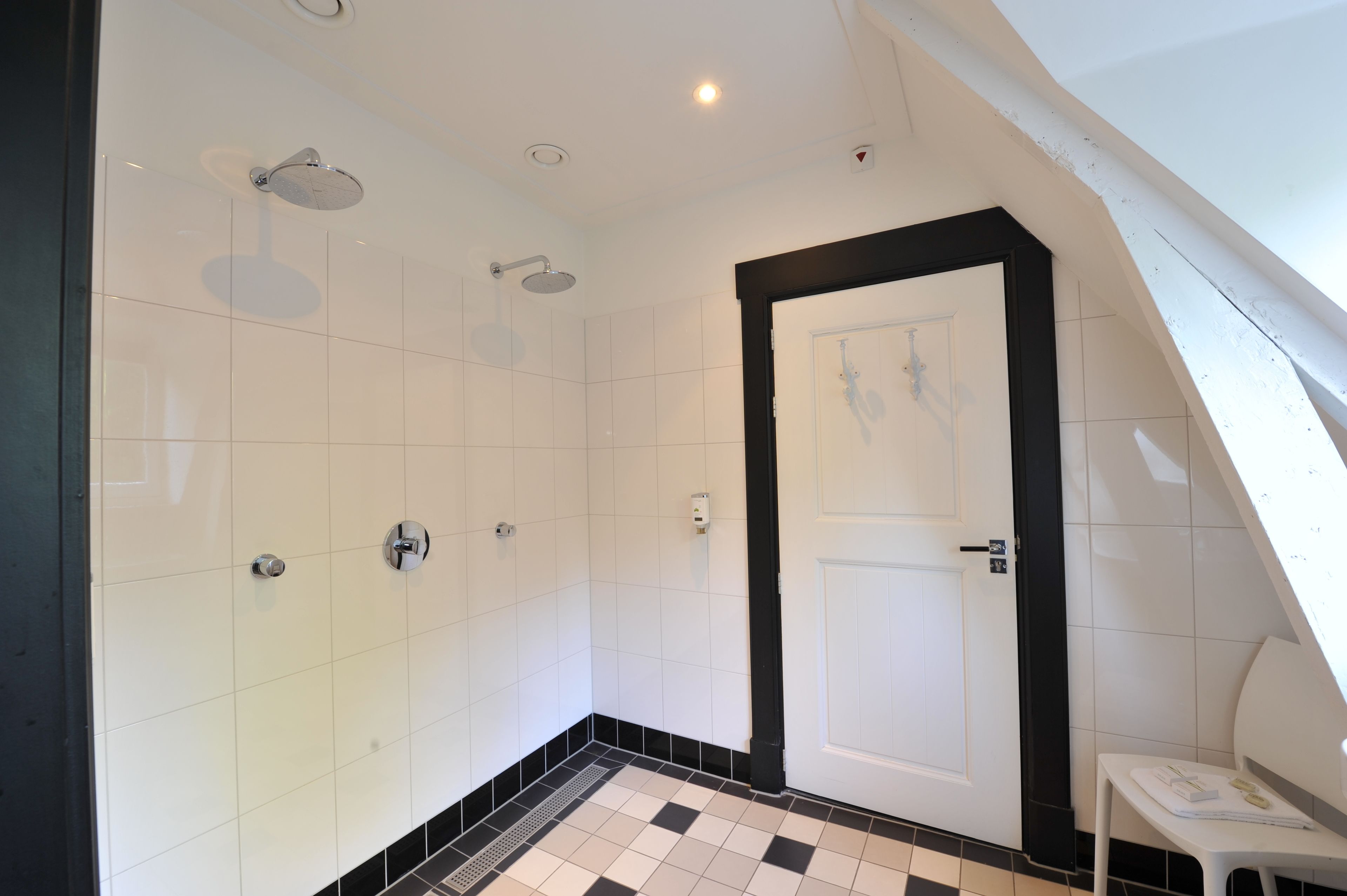 Un baño moderno con azulejos blancos, una puerta con marco negro y suelo de baldosas.