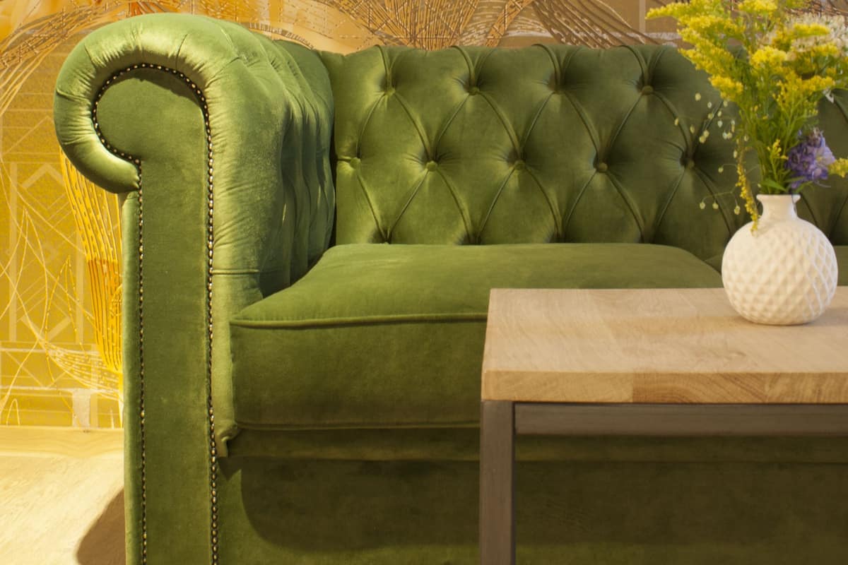 A green tufted sofa with a wooden coffee table in front.