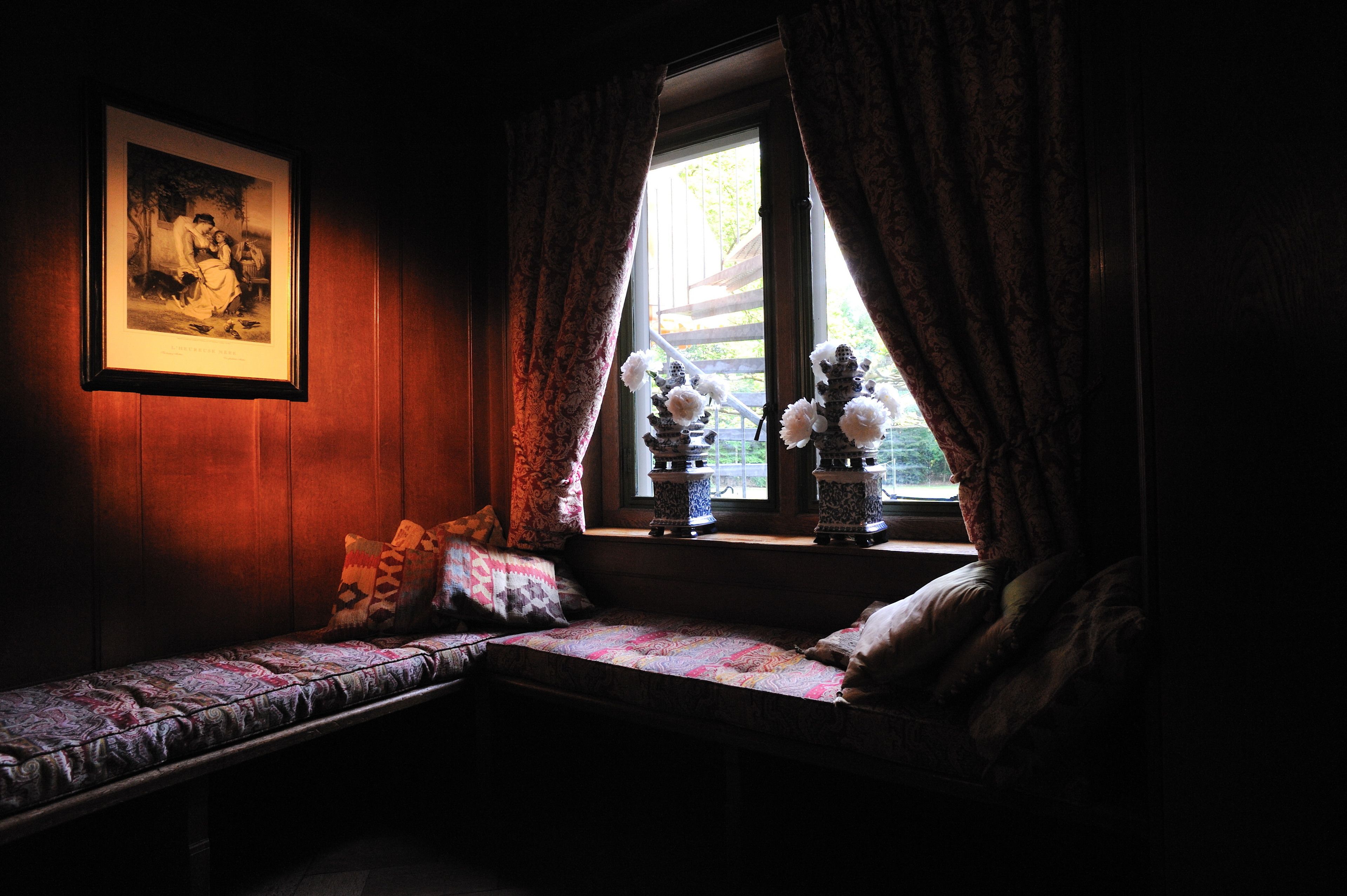 A dimly lit room with a bench, a framed picture on the wall, and a window with curtains.