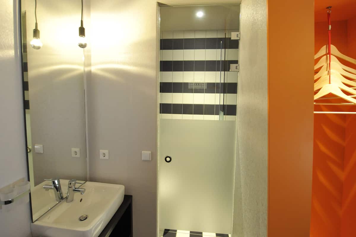 A bathroom with a sink, mirror, and a shower area with a tiled wall.