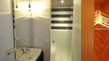Un baño con lavabo, espejo y zona de ducha con pared de azulejos.