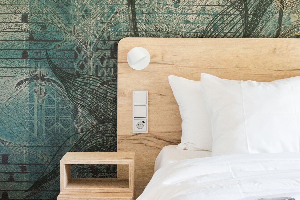 A neatly made bed with white linens, a wooden headboard, and a bedside table with a small drawer.