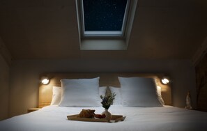 A bedroom with a skylight, a bed with white linens, two bedside lamps, and a tray with food and flowers on the bed. - Landgoed Huize Bergen (Vught)