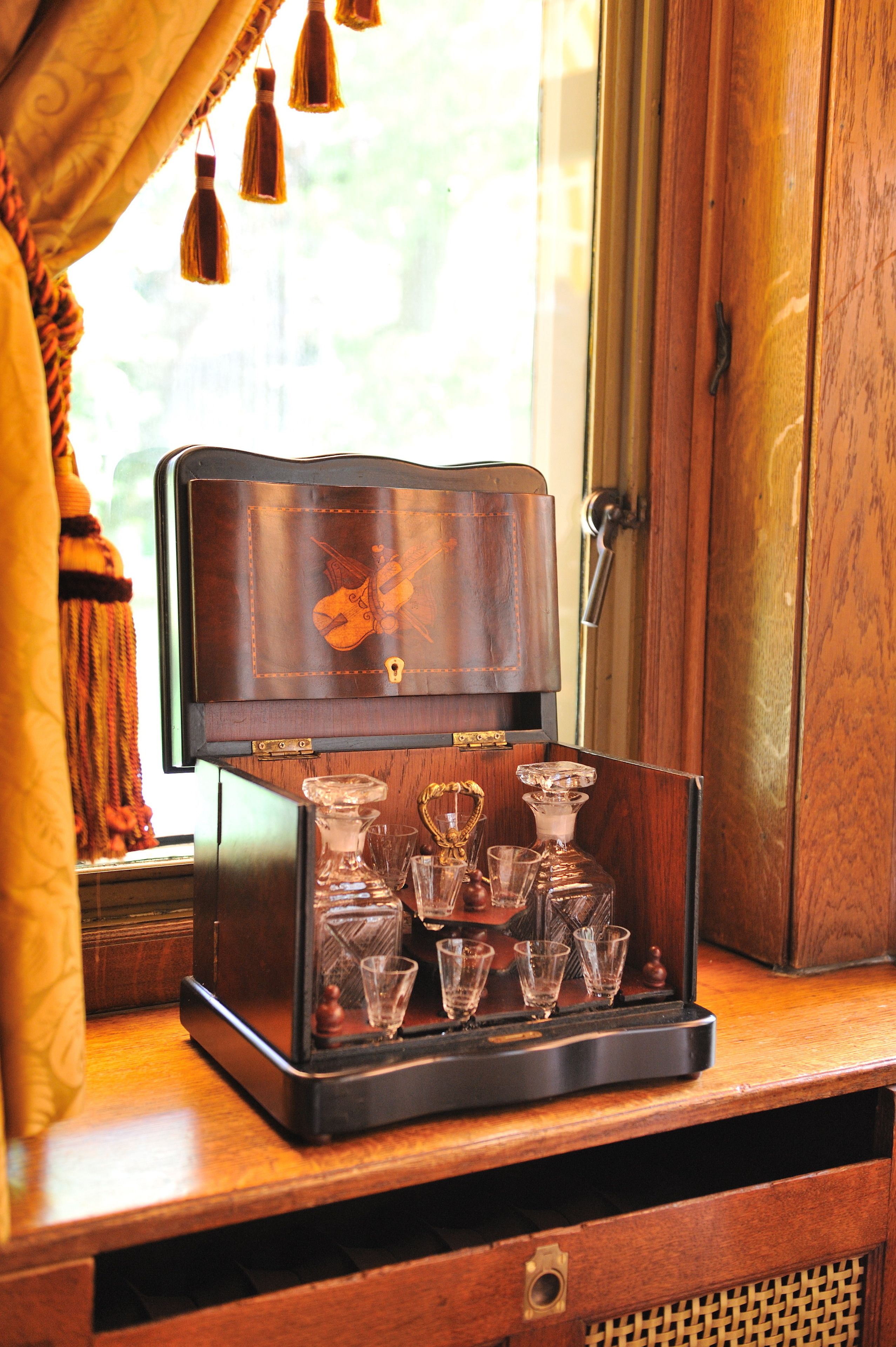 Un mobile in legno con decoro a violino, che contiene diversi decanter e bicchierini di vetro.