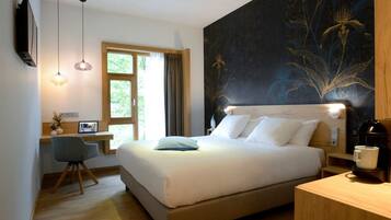 A modern hotel room with a large bed, a desk with a laptop, a coffee maker, and a wall with a floral design.