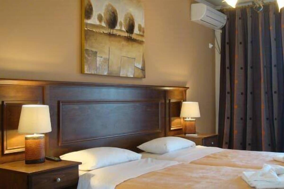 Una habitación de hotel con una cama grande, dos mesitas de noche con lámparas, un cuadro en la pared y una ventana con cortinas.