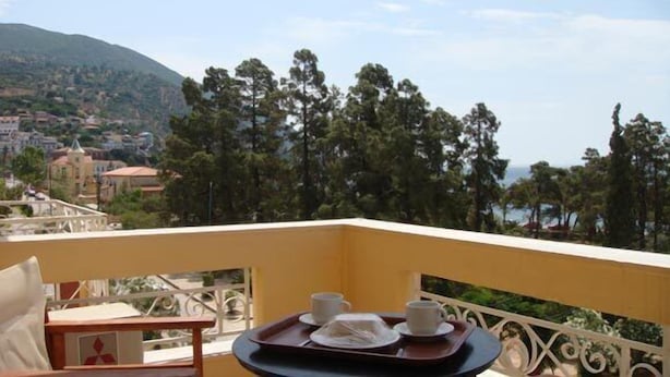 Un balcon avec une table dressée pour deux personnes, offrant une vue sur une ville côtière et les montagnes.