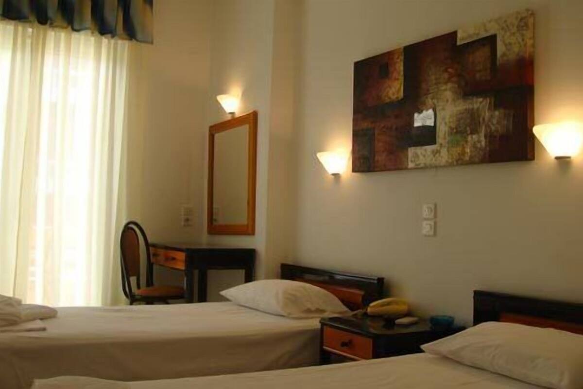 Una habitación de hotel con dos camas, un escritorio, una silla y un cuadro en la pared.