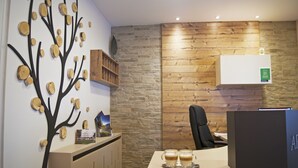 A reception desk with a wooden wall, a tree decal, and a coffee station. - Rooms & Apartments Kepic (Cerklje na Gorenjskem)