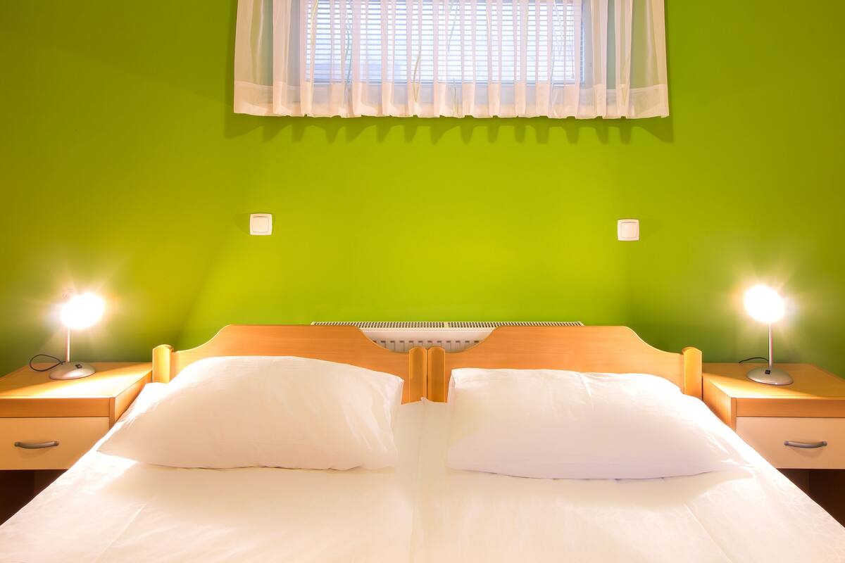 A bed with white linens, two bedside tables with lamps, and a window with a white curtain.