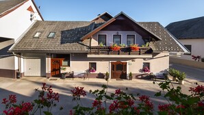 A two-story building with a sloped roof, a balcony with potted plants, and a front door. - Rooms & Apartments Kepic (Cerklje na Gorenjskem)