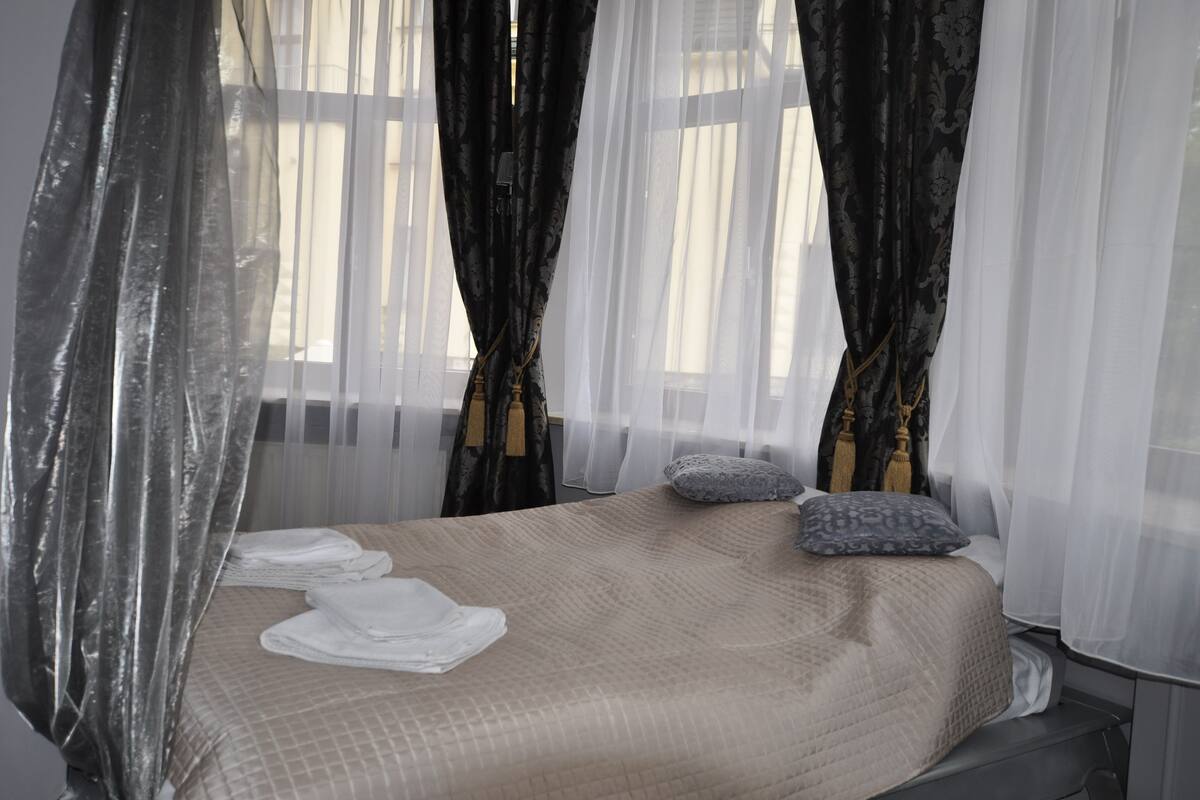 A neatly made bed with a beige quilt, two pillows, and a mosquito net.