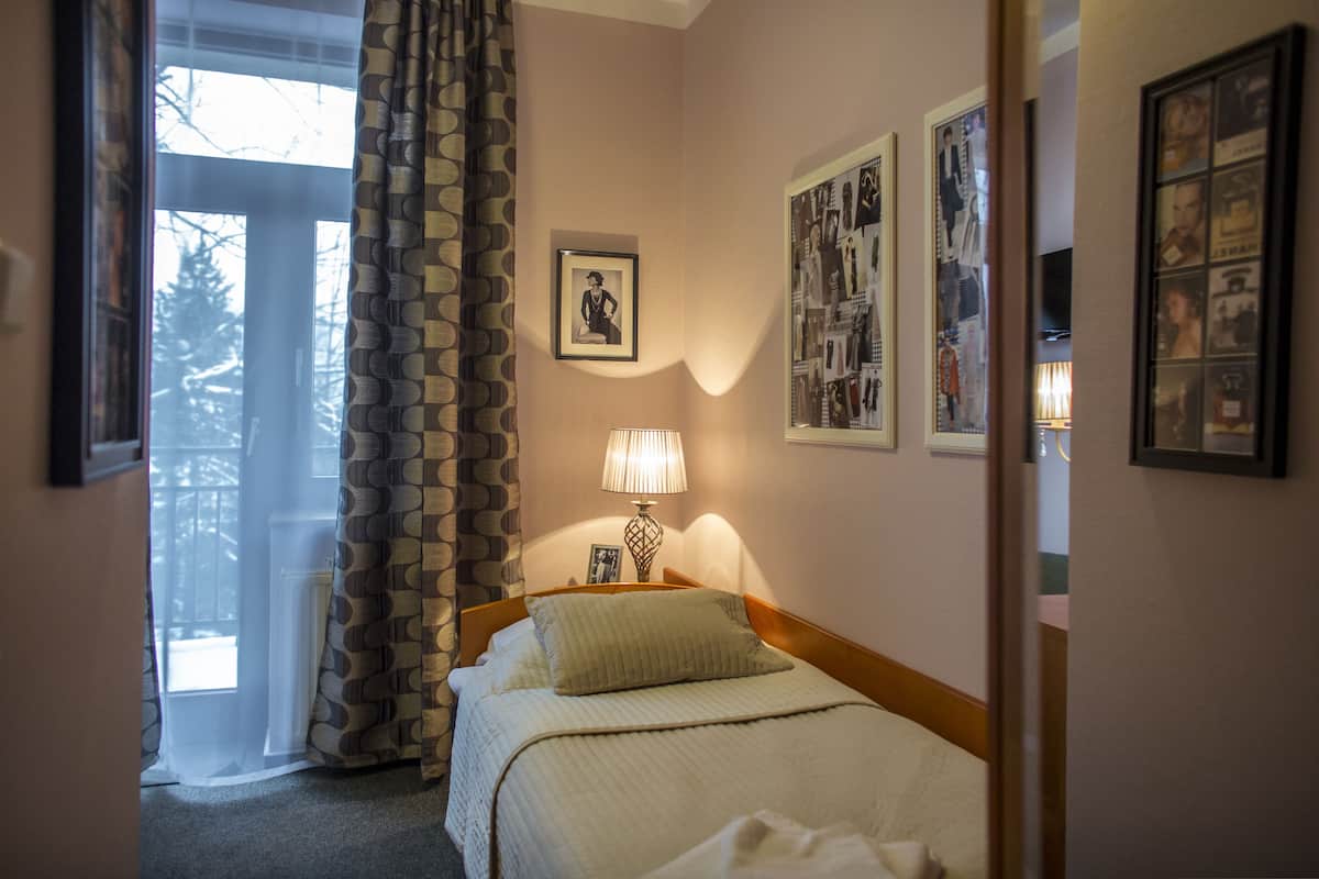 A hotel room with a bed, a lamp, a framed picture on the wall, and a window with curtains.