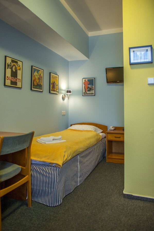 A hotel room with a bed, a desk, a chair, and a television on the wall.