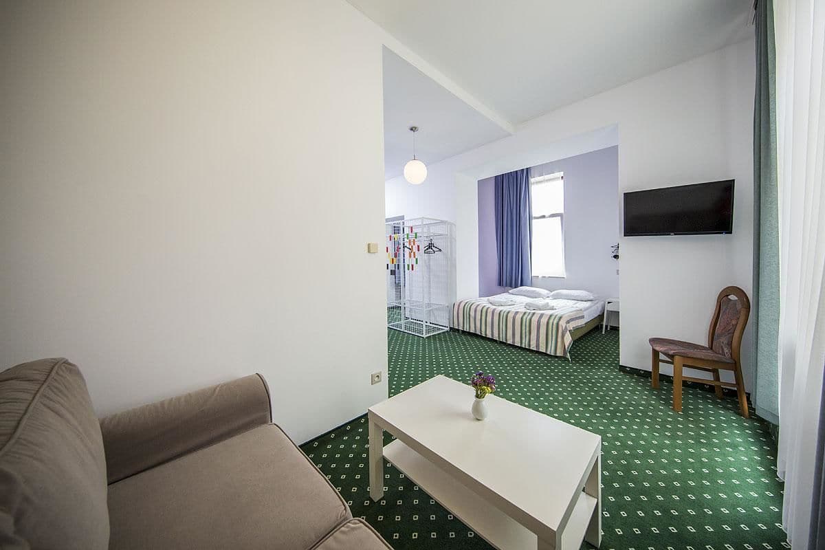 A hotel room with a bed, a TV, a chair, a table, and a small balcony area.