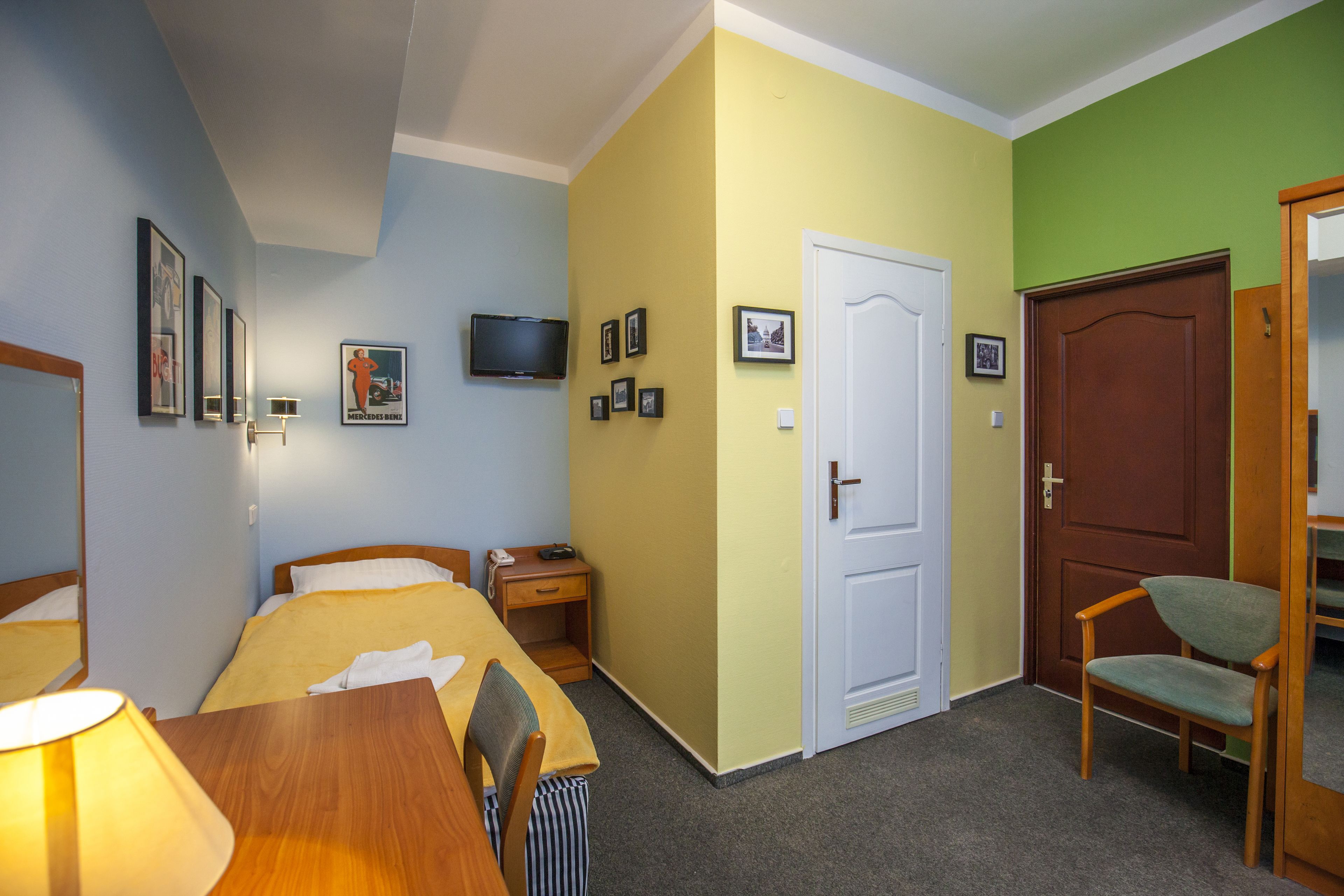 Una habitación de hotel con cama, mesita de noche, lámpara, silla, televisor y puerta.