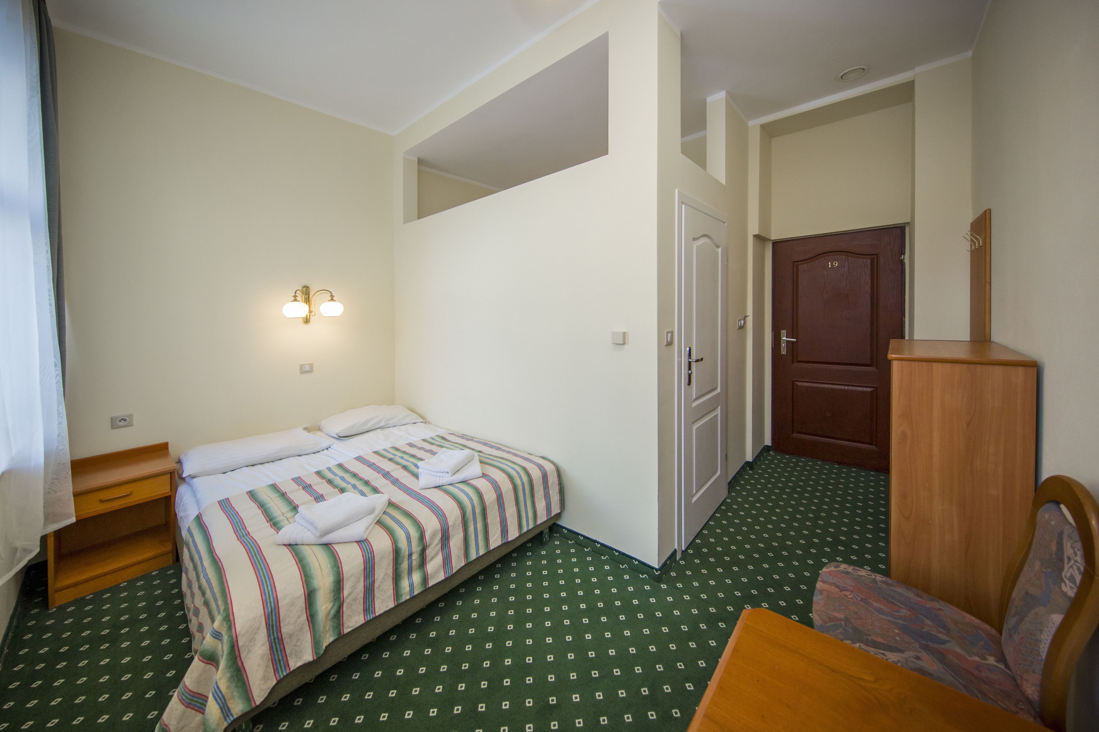 A hotel room with a bed, a nightstand, a chair, a wooden cabinet, and a door.