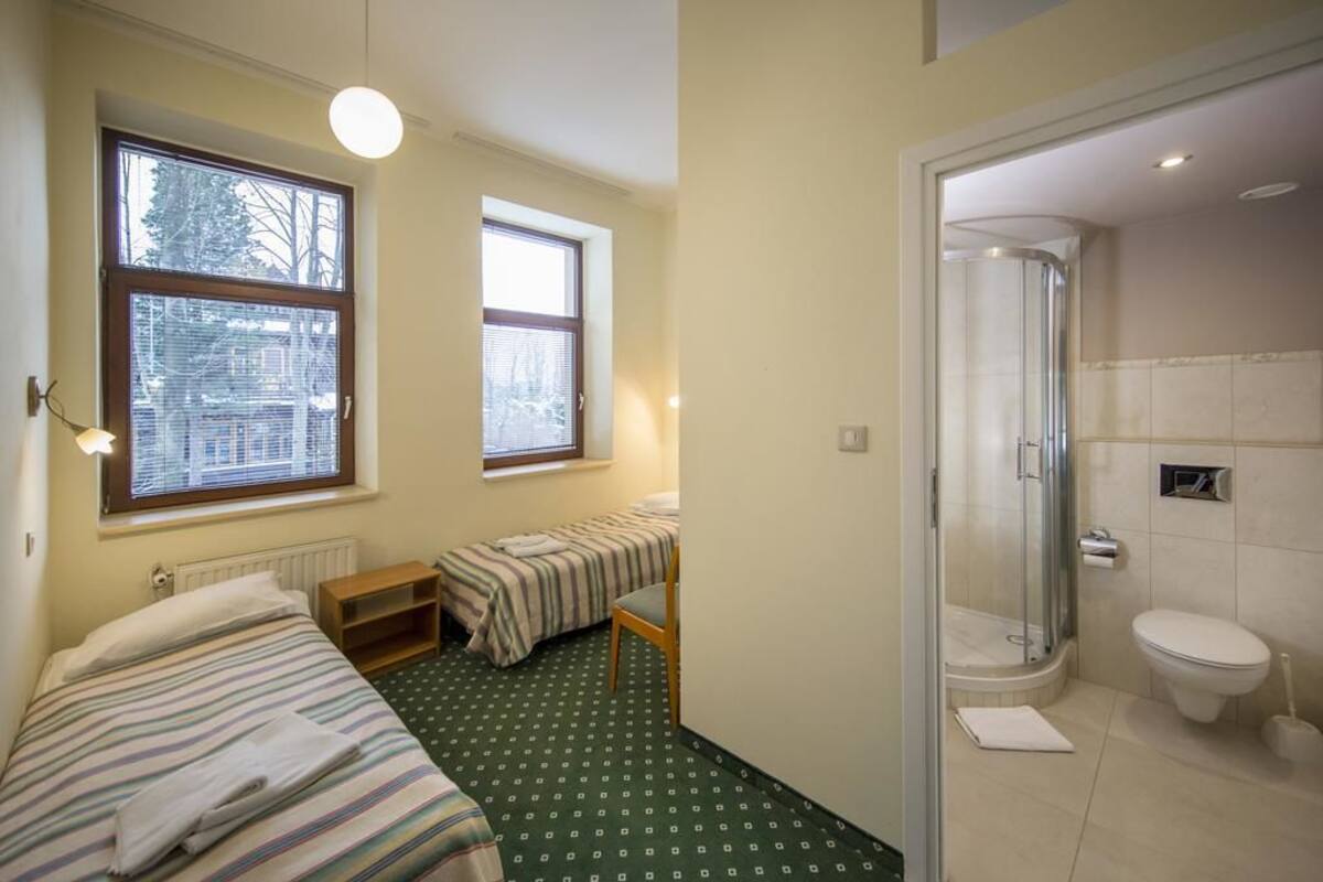 A small, well-lit room with two beds, a shower, and a toilet.