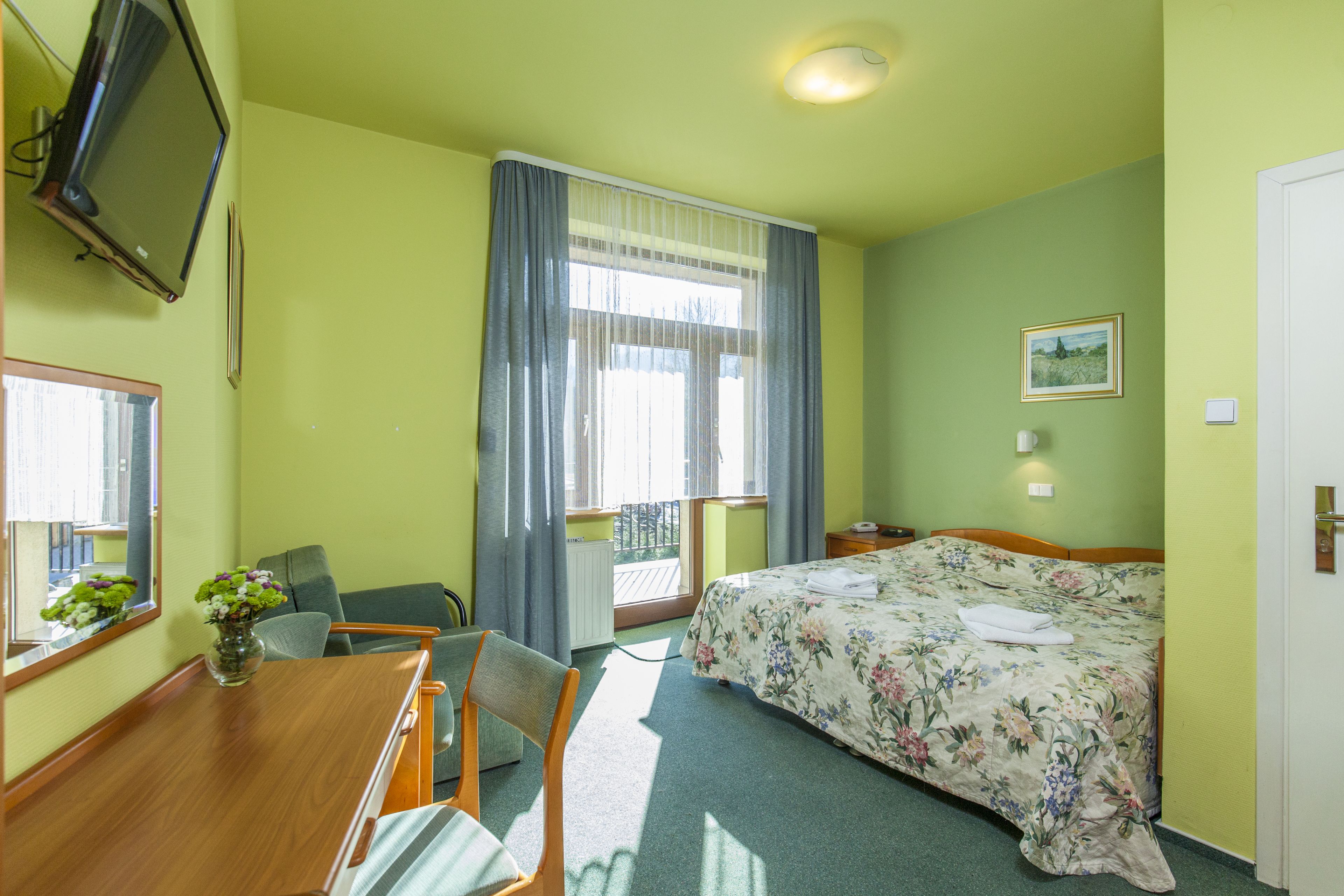 A hotel room with a bed, a desk, a chair, a television, and a window with curtains.