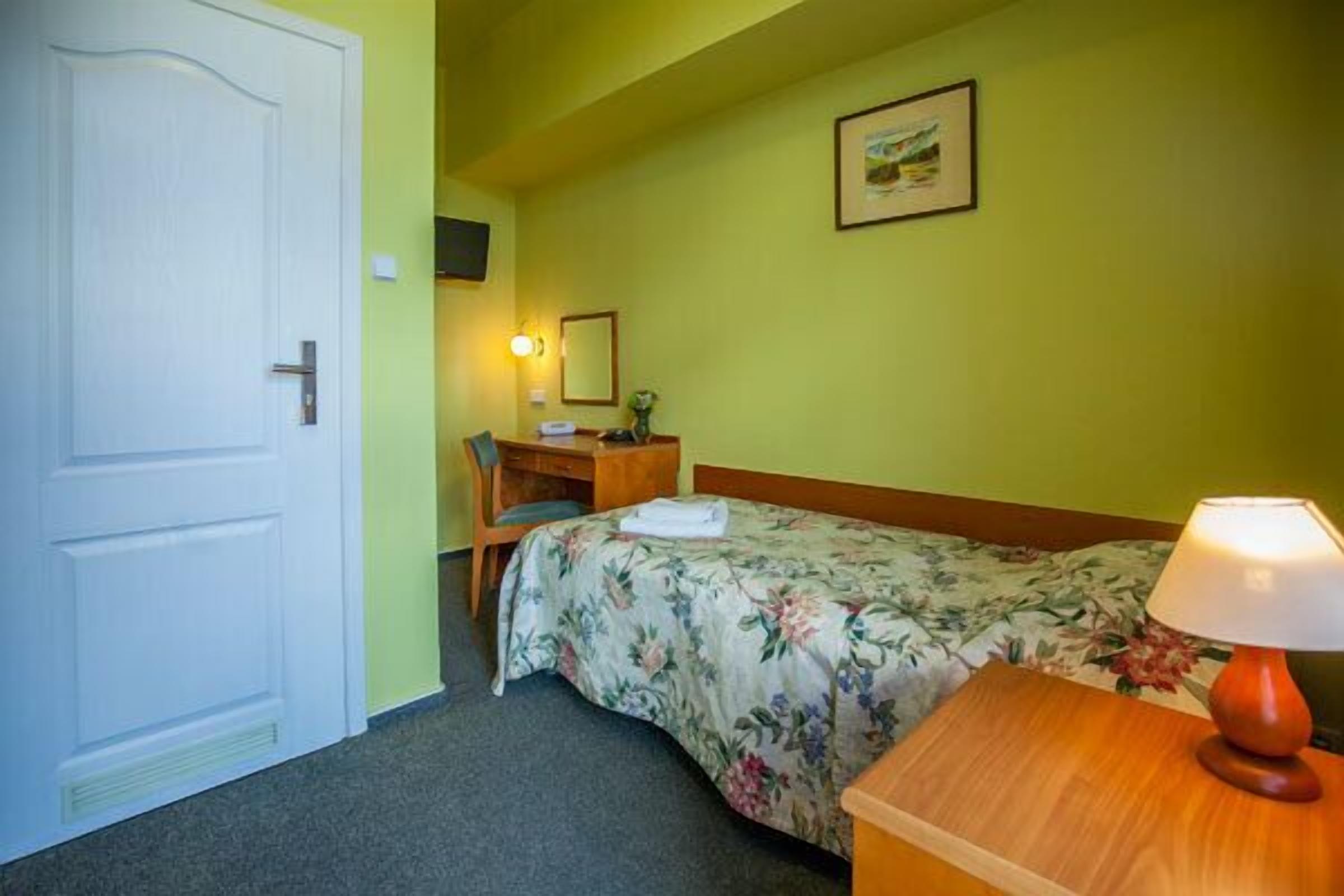 Una camera d'albergo con un letto, una scrivania, una sedia, una lampada e una porta.