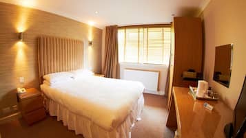 A hotel room with a large bed, bedside lamps, a desk with a computer, a window with curtains, and a radiator.