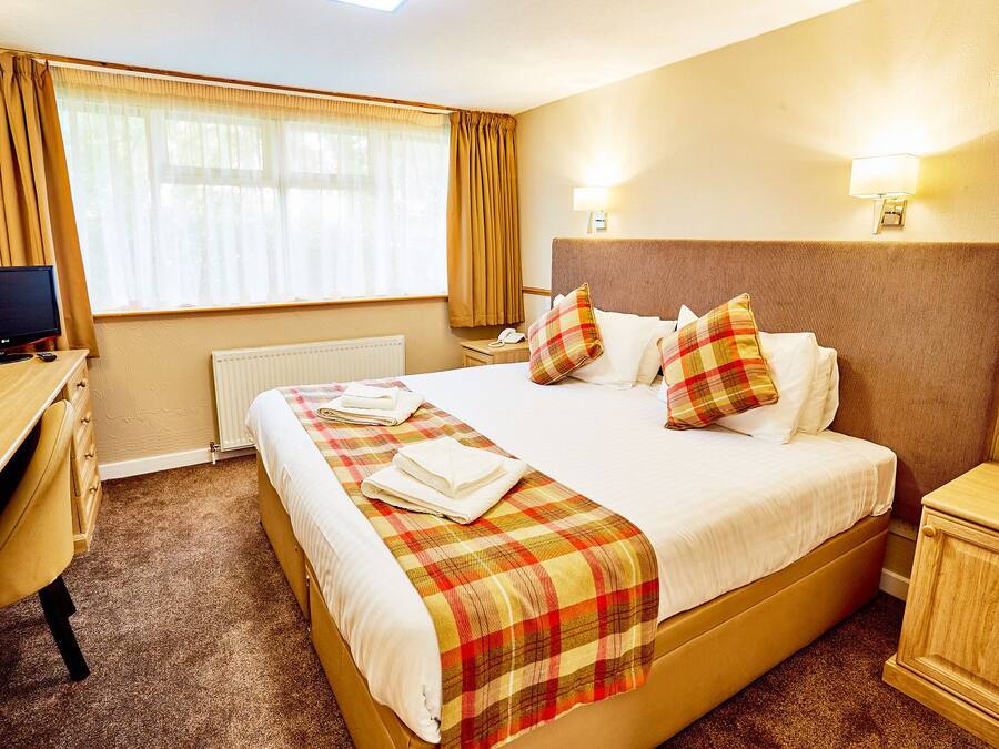 A hotel room with a bed, a desk, a chair, a TV, and a window with curtains.
