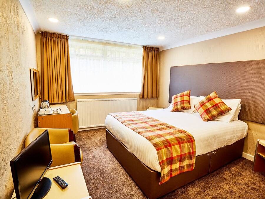 Una habitación de hotel con una cama, un escritorio con computadora, una silla y un televisor.