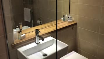 Une salle de bain avec un lavabo blanc, des toilettes, un miroir et un espace douche.