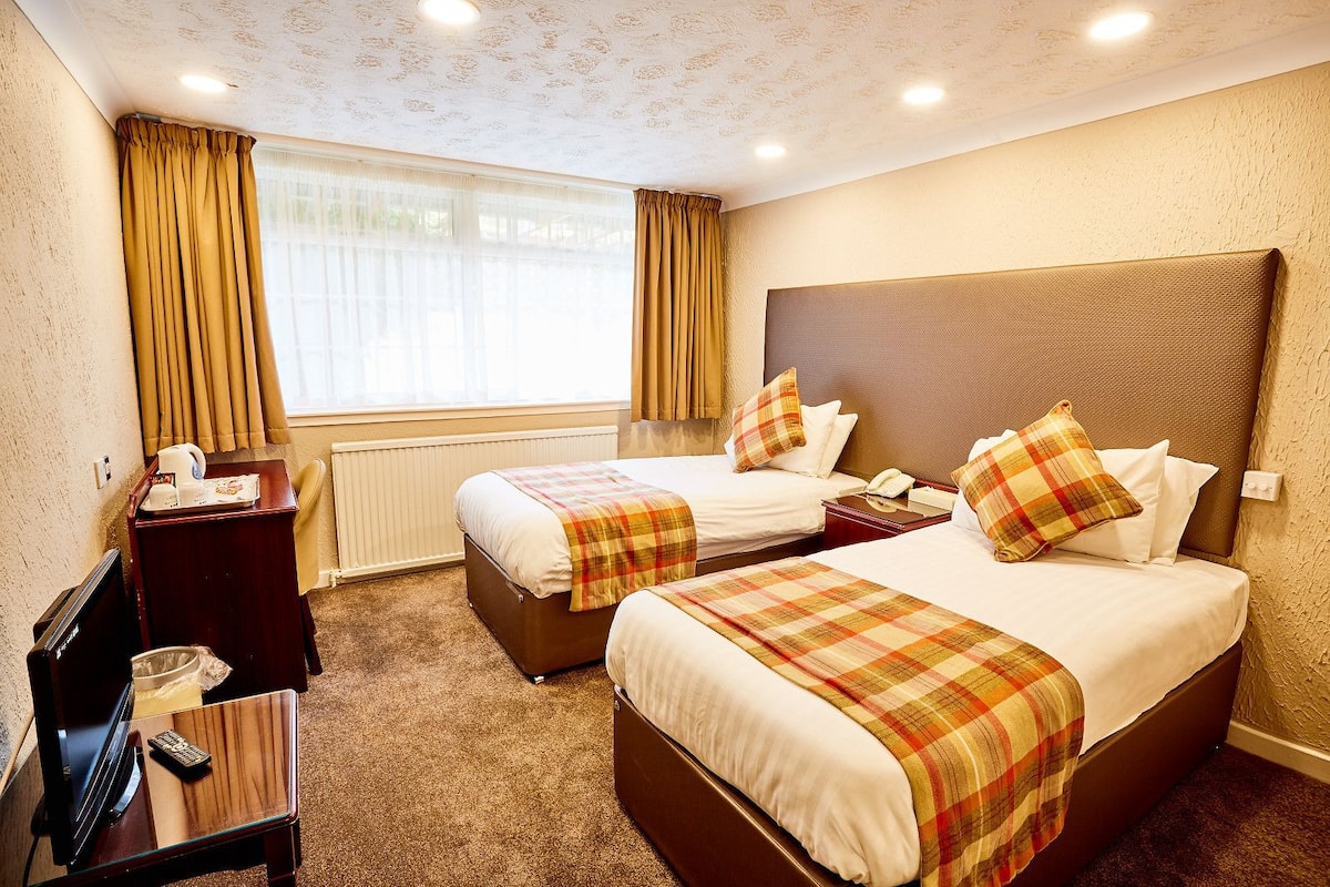 A hotel room with two beds, a desk with a telephone, a coffee maker, and a television.