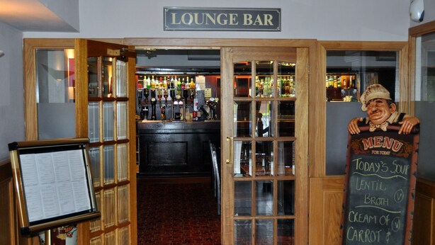 A lounge bar with a wooden interior, a menu board, and a bar counter with various bottles. - Abbotsford Hotel (Dumbarton)