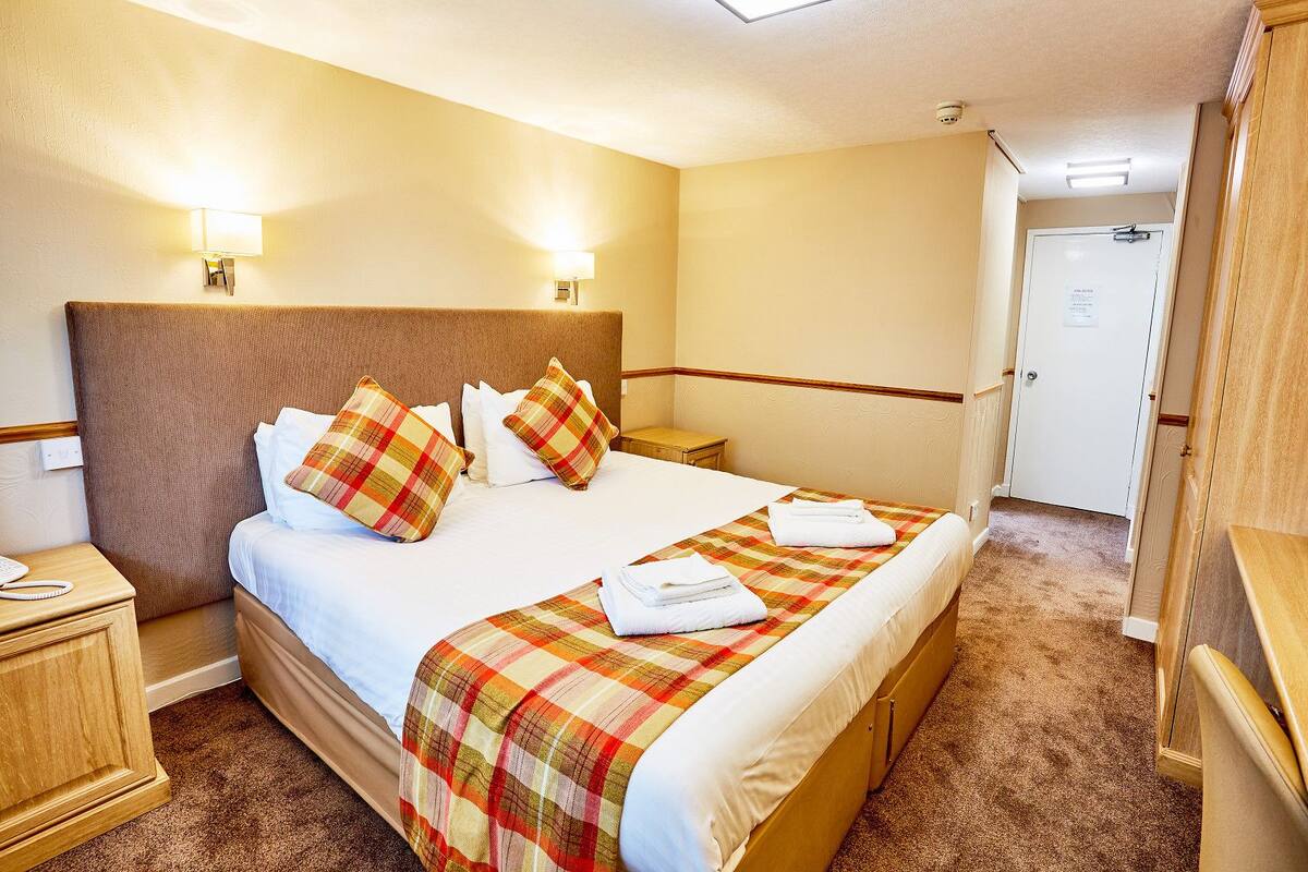 A hotel room with a large bed, two bedside tables, a headboard, and a door.