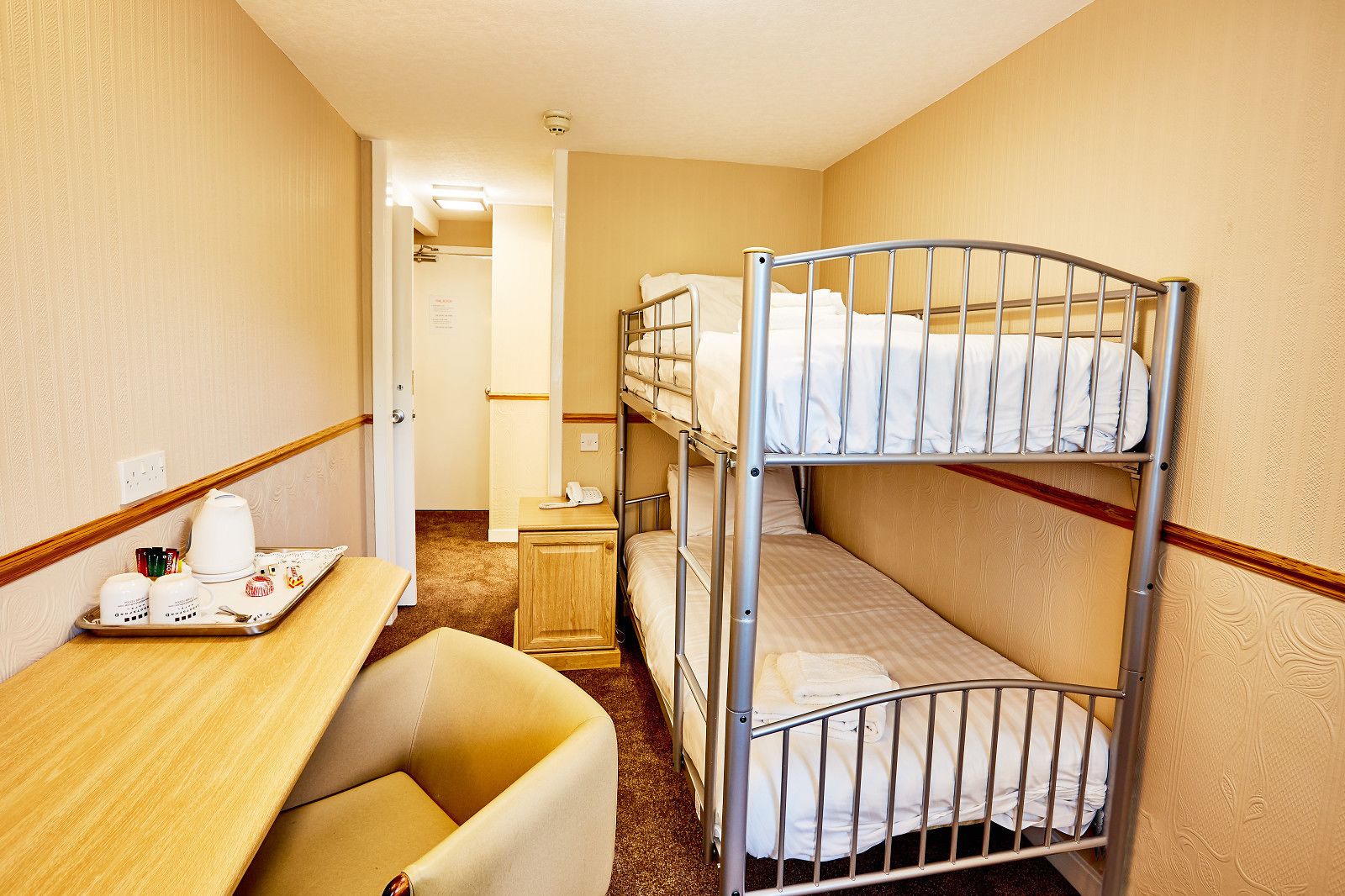A bunk bed room with a desk, chair, and a tray with breakfast items.