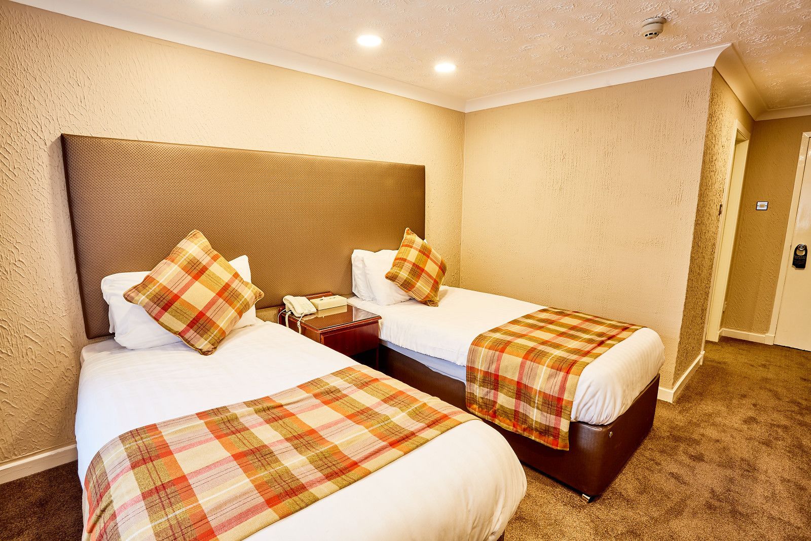 A hotel room with two beds, each with a headboard, a nightstand, and a telephone.