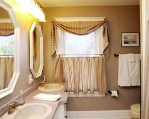 A bathroom with two sinks, a mirror, a window with curtains, a toilet, and a towel rack.