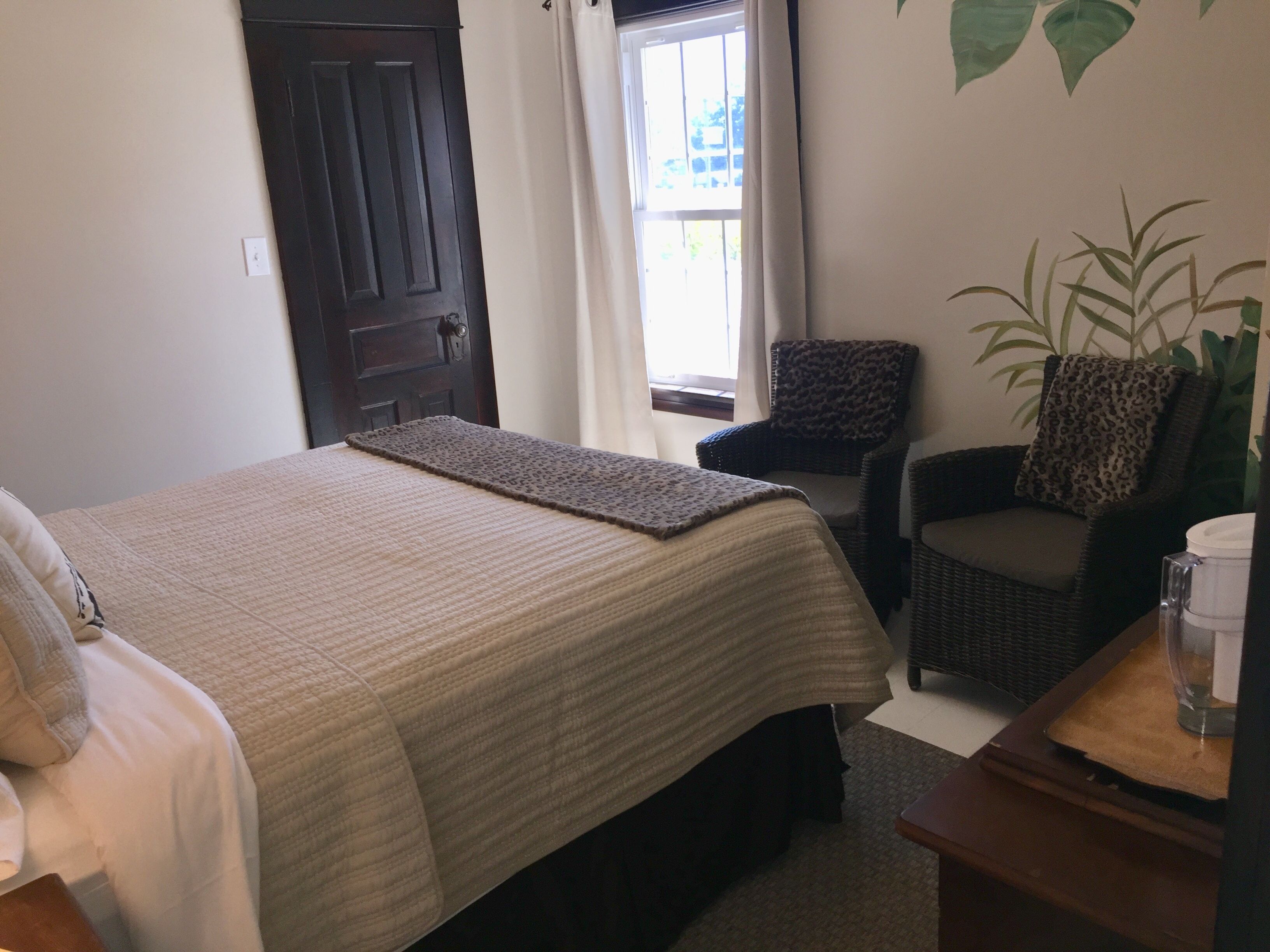 A bedroom with a bed, a chair, a plant, and a window with curtains.