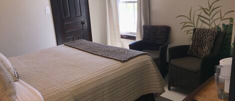 A bedroom with a bed, a chair, a plant, and a window with curtains.