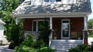 A two-story house with a front porch, a chimney, and a number 20 sign. - Simcoe Suites on the Henley B&B (St. Catharines)
