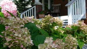 A house with a brick exterior, white porch railing, and a potted plant on the porch. - Simcoe Suites on the Henley B&B (St. Catharines)