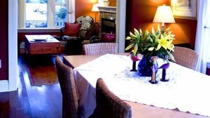 A dining area with a table set for four, a chandelier above, and a view of the living room through an open doorway. - Simcoe Suites on the Henley B&B (St. Catharines)
