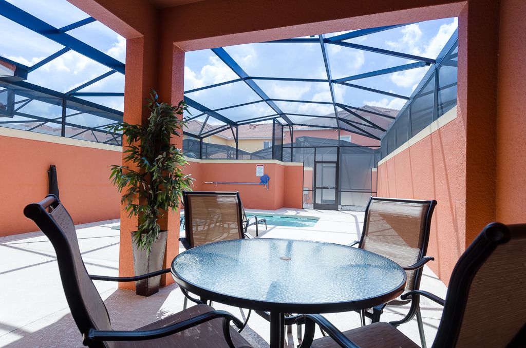 A covered outdoor area with a glass table and chairs, a pool, and a potted plant.