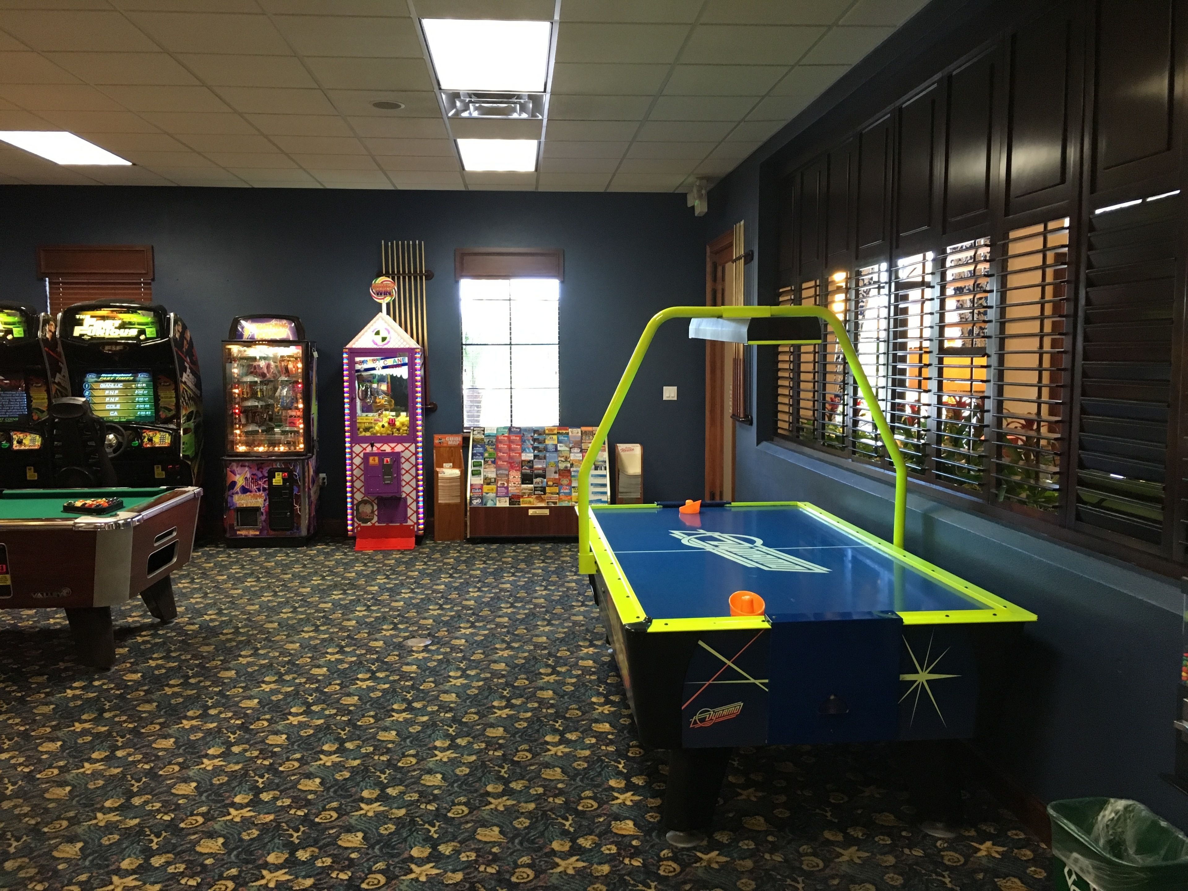 A room with a pool table, arcade machines, and a vending machine.