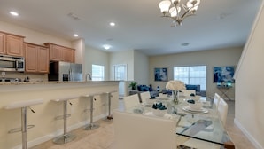 A modern kitchen with stainless steel appliances, a bar area with stools, and a dining area with a glass table and chairs.