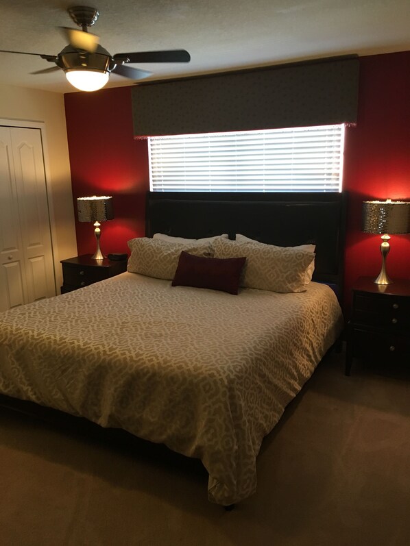 Quarto com cama, duas luminárias de cabeceira, ventilador de teto e janela com persianas.