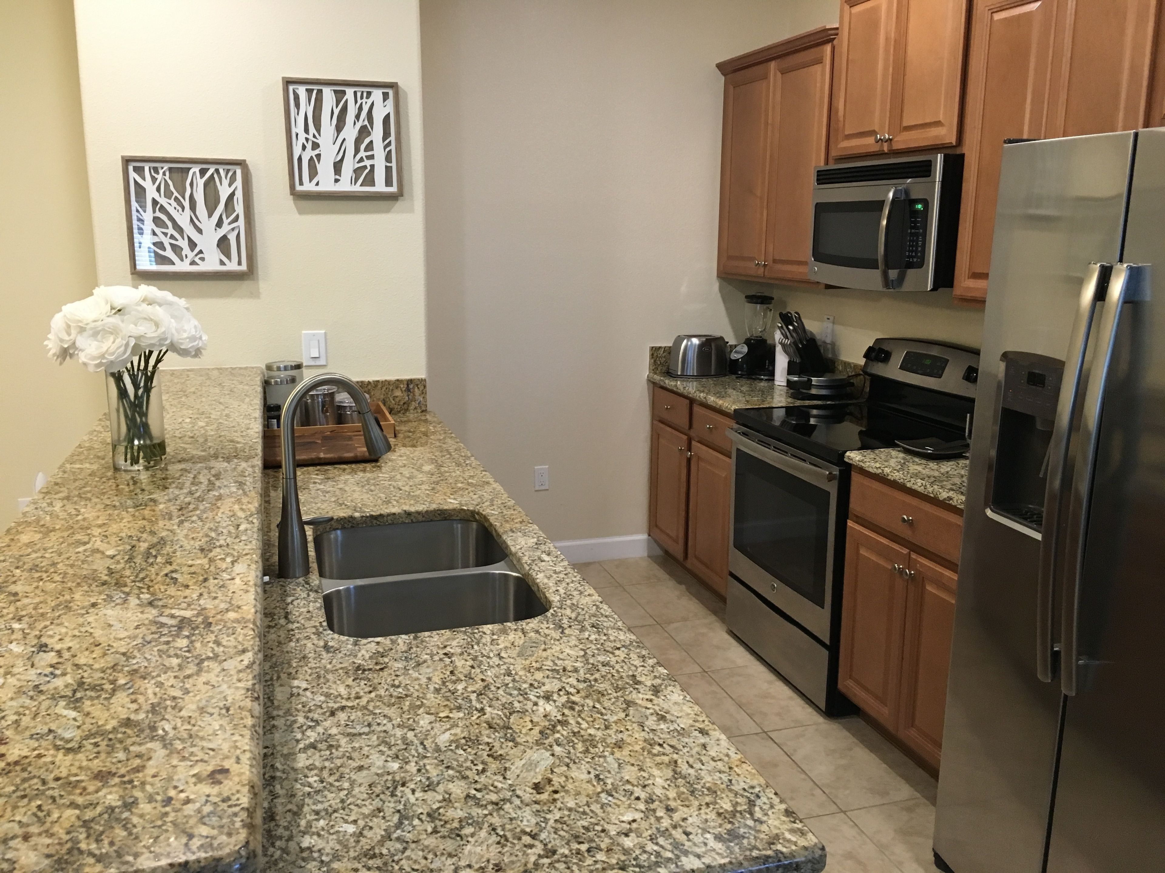 A kitchen with granite countertops, stainless steel appliances, wooden cabinets, and decorative wall art.