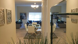 A modern living room with a dining area, a chandelier, and a large mirror.