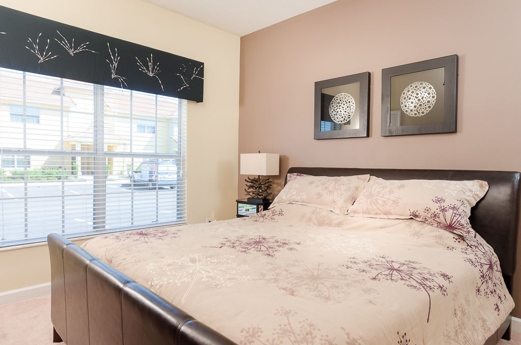 A bedroom with a large bed, a window with blinds, and two wall-mounted decorative mirrors.